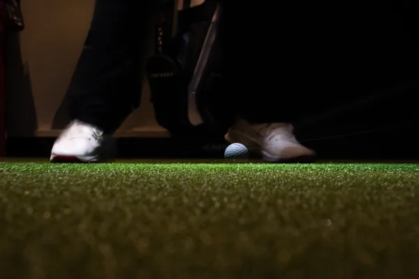 Golfball auf der Hitting-Mat — Spielerfüße im Anlauf